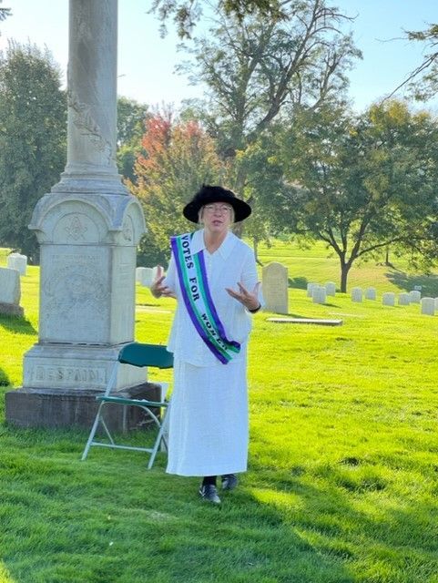 A woman wearing a sash that says love is peace is standing in a cemetery