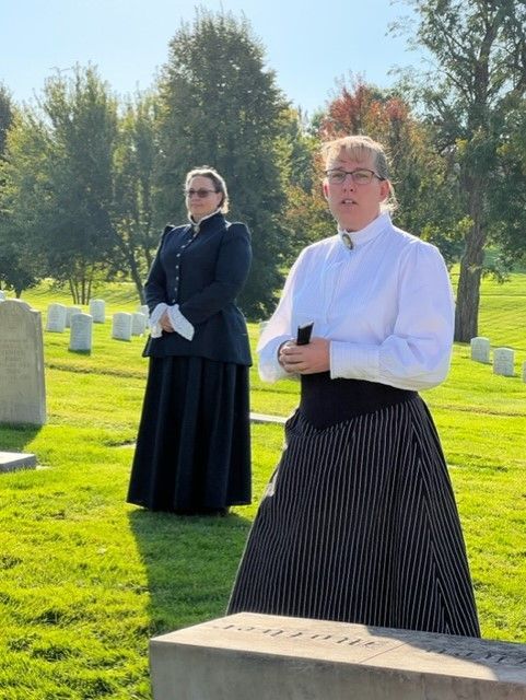 A woman standing in a cemetery with a sash that says love is peace
