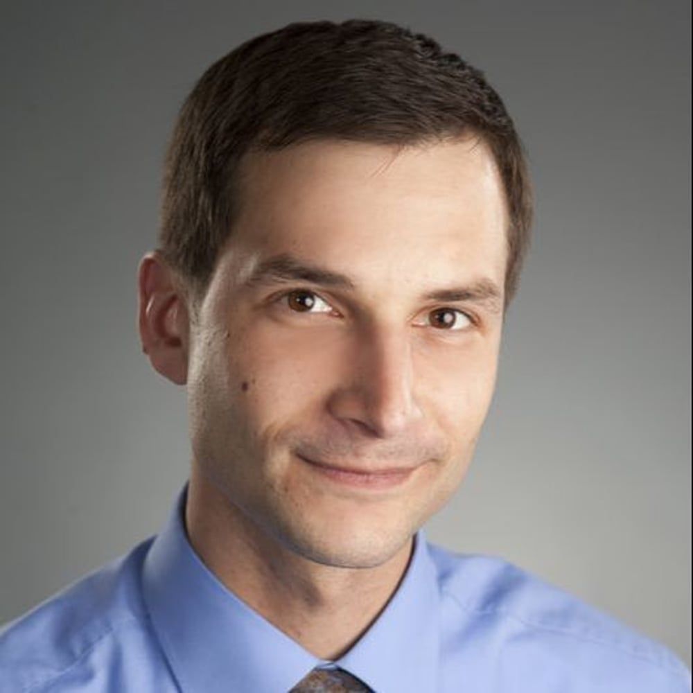 A man in a blue shirt and tie smiles for the camera