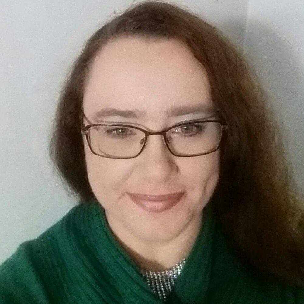A woman wearing glasses and a green sweater is smiling for the camera.