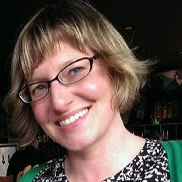 A woman wearing glasses and a green shirt is smiling.