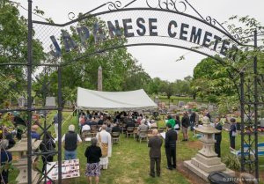 A group of people are gathered in a cemetery under a sign that says japanese cemetery.
