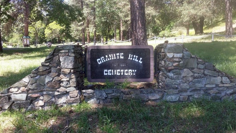 A sign for granite hill cemetery is sitting on top of a stone wall.