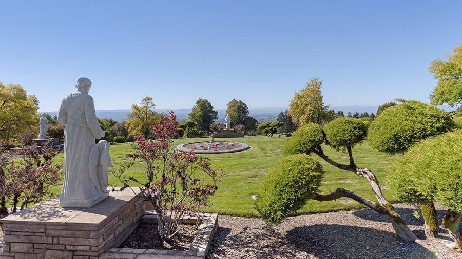 A statue of jesus is sitting on top of a brick wall in a cemetery.