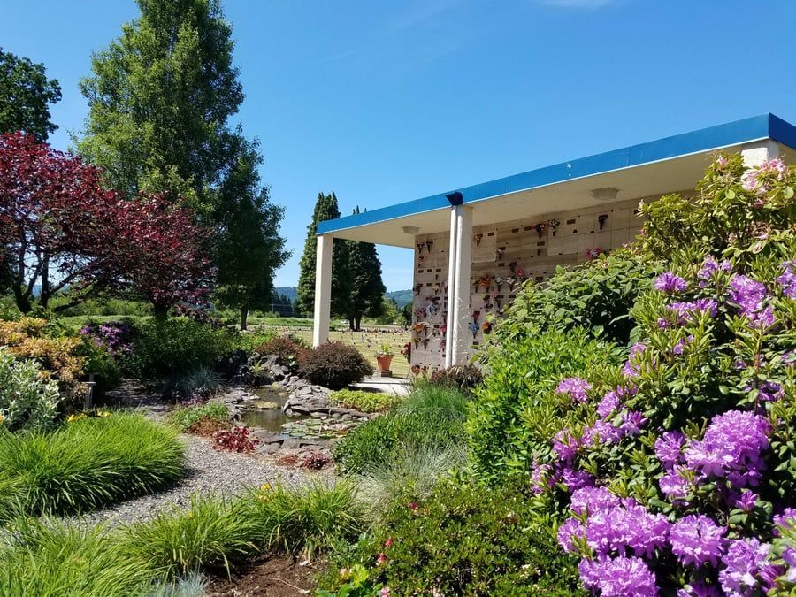 A building with a blue roof is surrounded by purple flowers and trees.