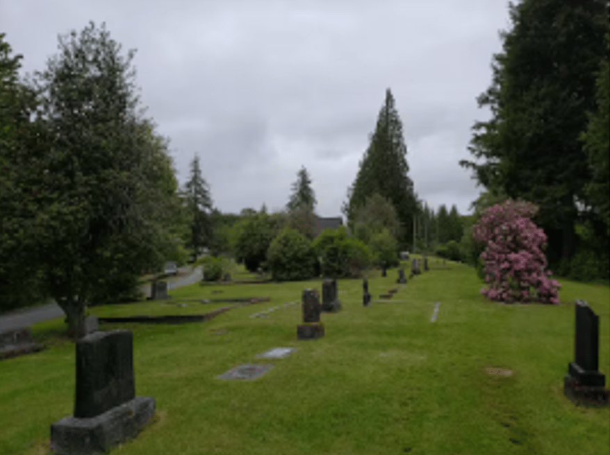 A cemetery with many graves and trees on a cloudy day