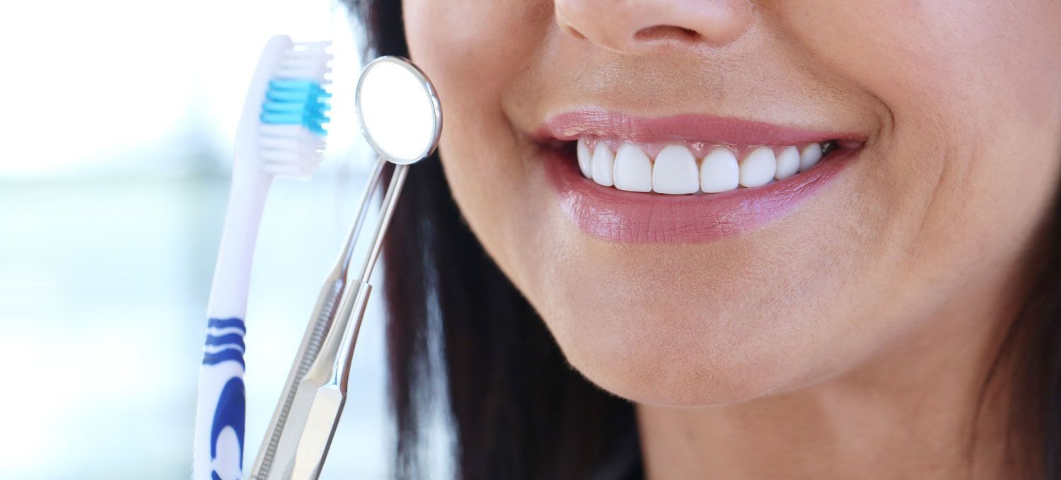 A woman is brushing her teeth with a toothbrush and a mirror.