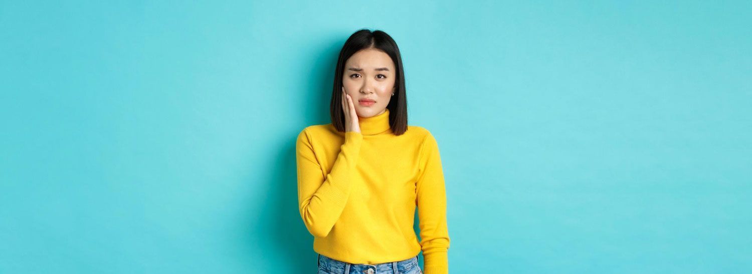 A woman in a yellow sweater is covering her mouth with her hand.