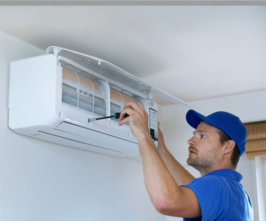 A man is fixing an air conditioner with a screwdriver.