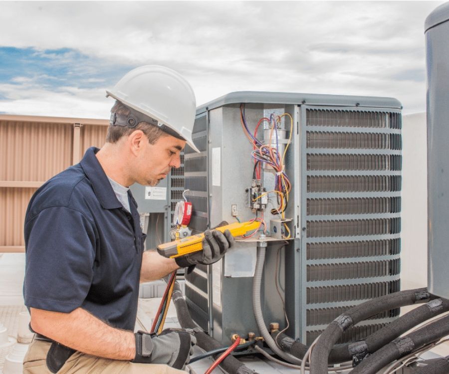 A man wearing a hard hat is working on an air conditioner.
