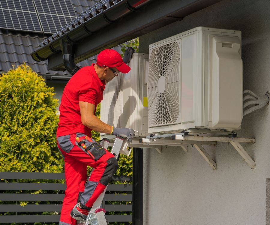A man is installing an air conditioner on the side of a house.
