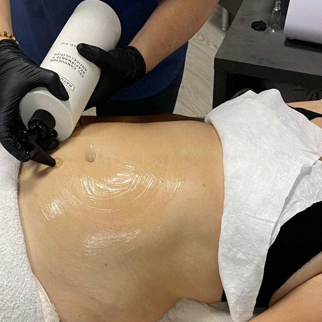 Persona con guantes negros aplicando crema en el abdomen de otra persona.