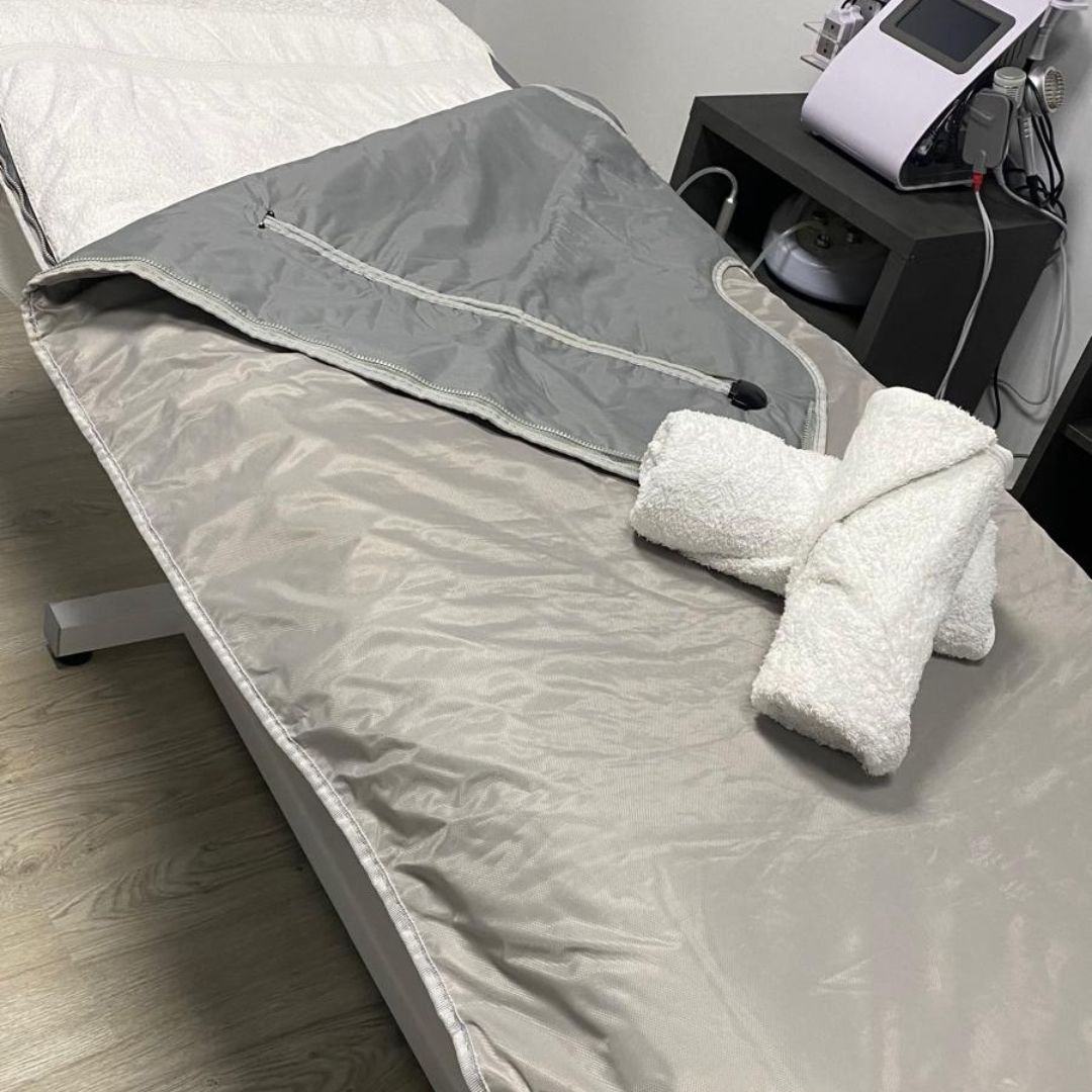 Camilla de tratamiento con manta gris, toallas blancas y equipo médico en un entorno de spa.