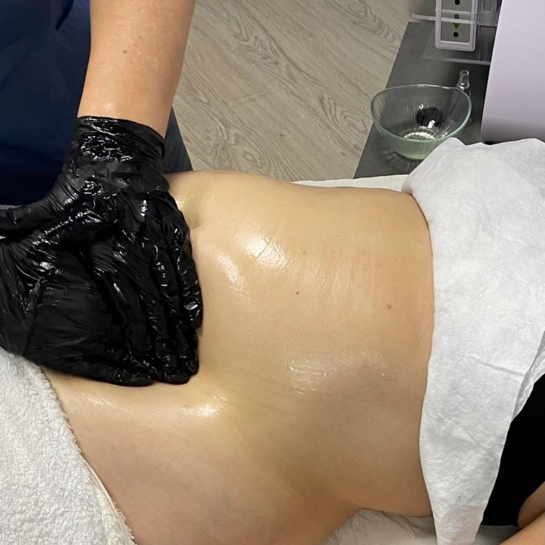 Persona recibiendo un masaje abdominal con manos enguantadas. Piel brillante y aceitosa sobre una camilla de masaje.