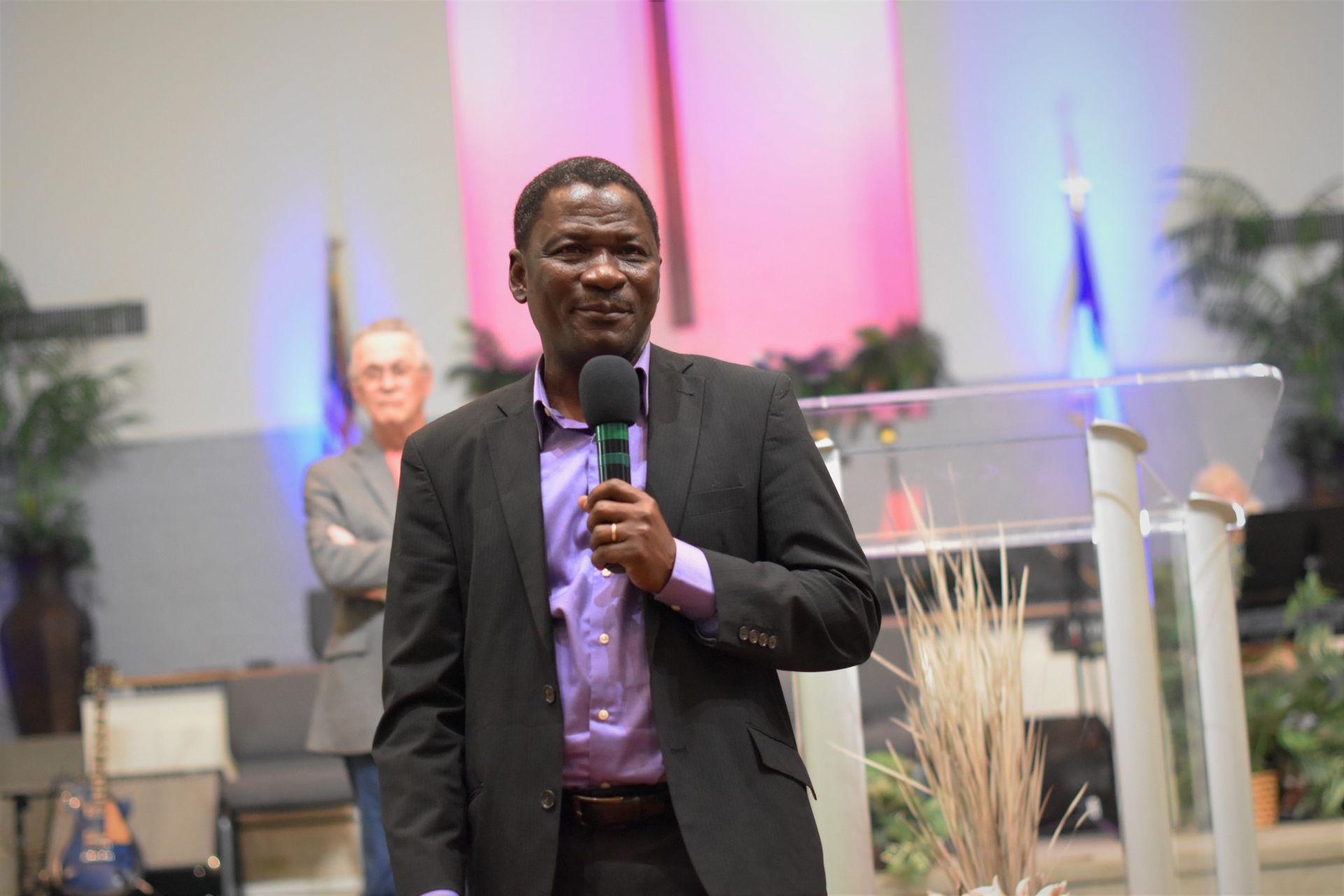 A man in a suit is standing in front of a podium holding a microphone.