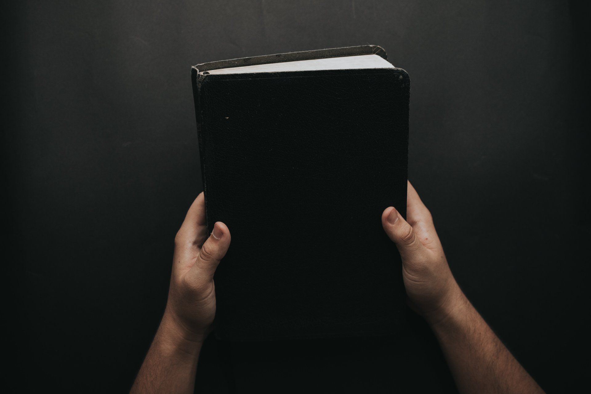 A person is holding a black bible in their hands.
