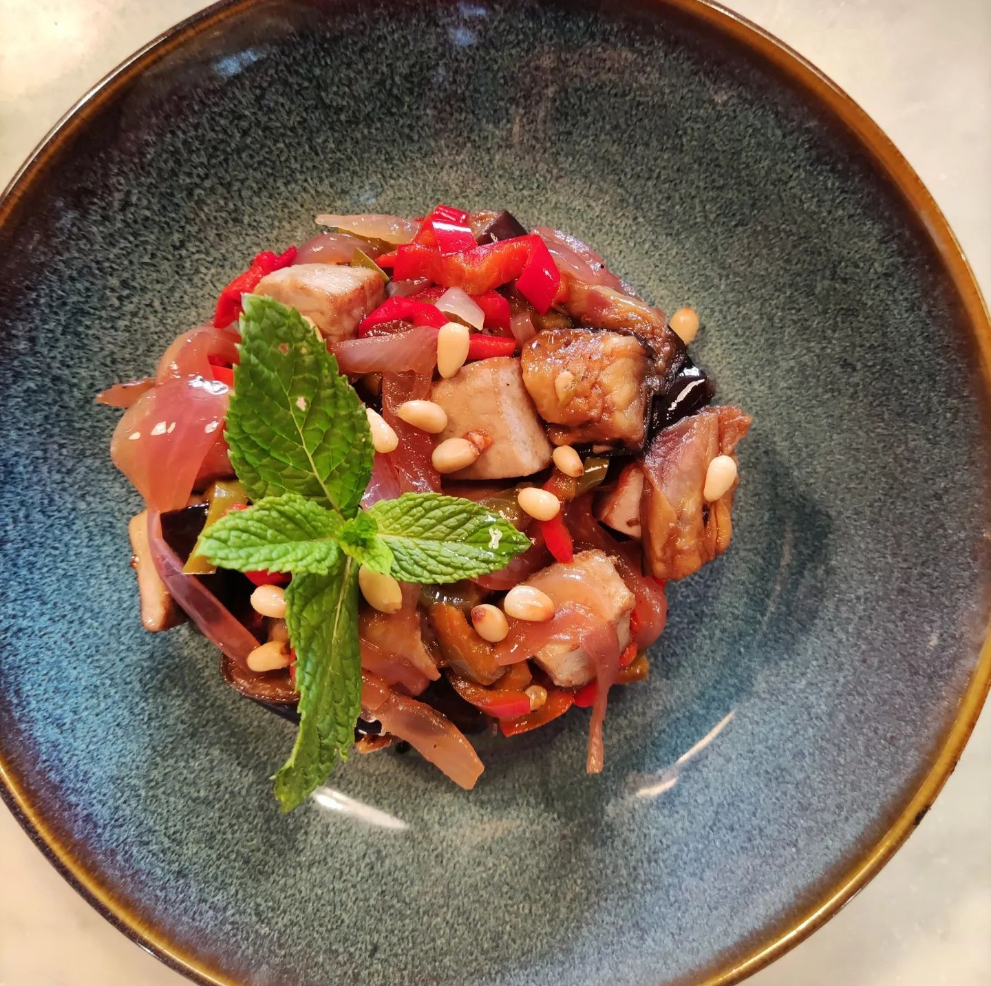 Caponata di melanzane in una ciotola verde acqua, guarnita con menta e pinoli.