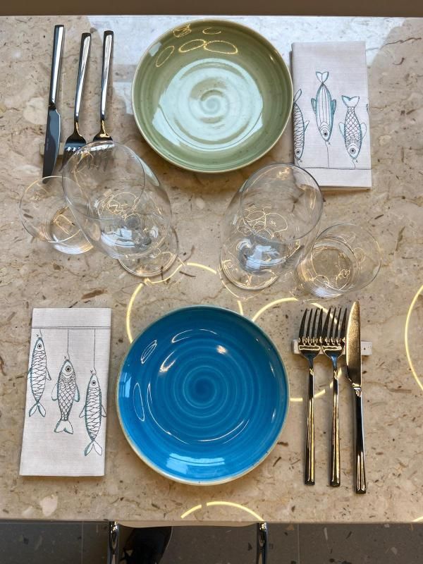 Apparecchiatura della tavola con piatti, bicchieri, posate e tovaglioli con stampe di pesci blu e verdi.