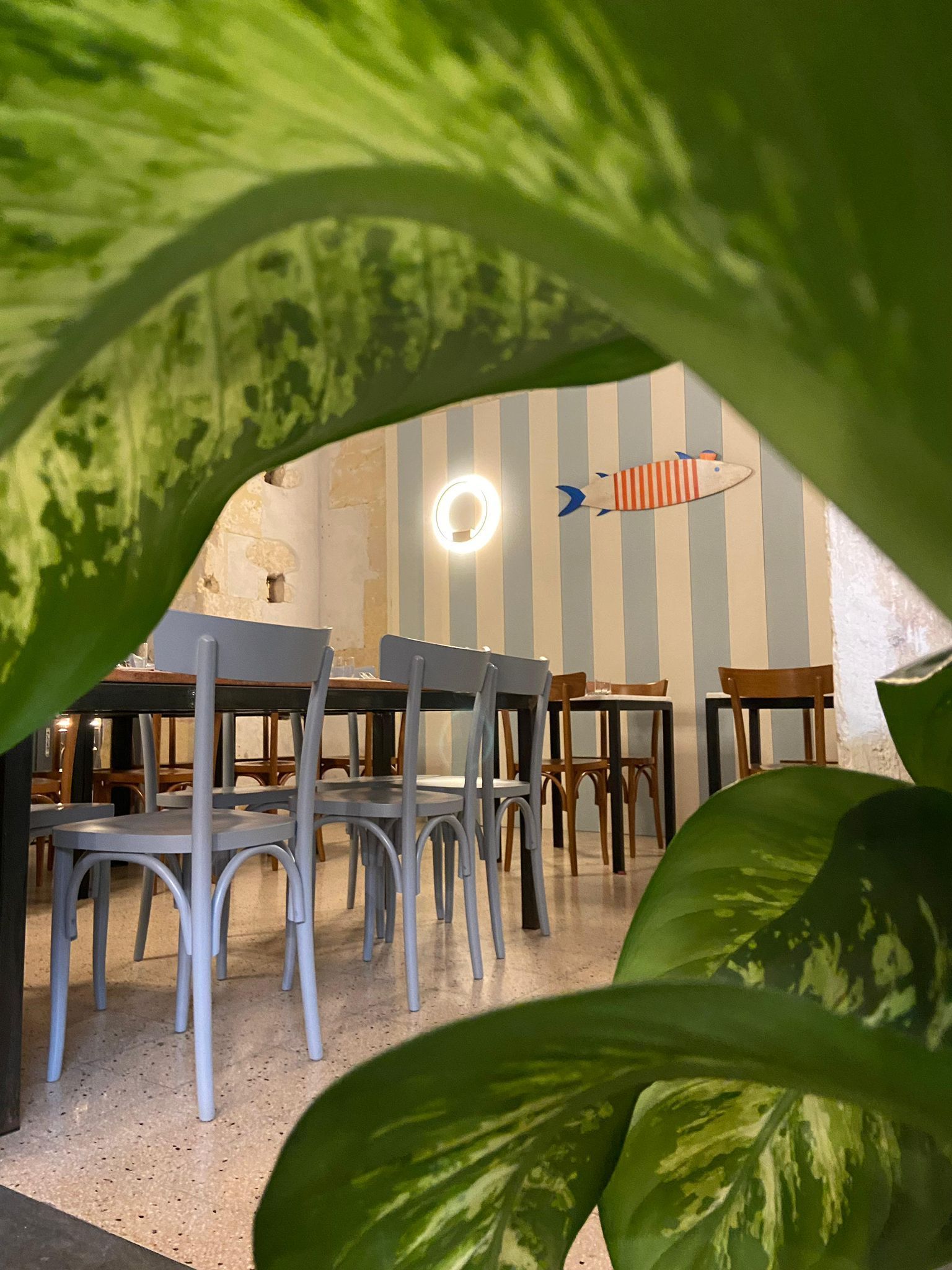 Interno di un ristorante con tavoli apparecchiati, decorazioni a forma di pesce sulle pareti e fiori.