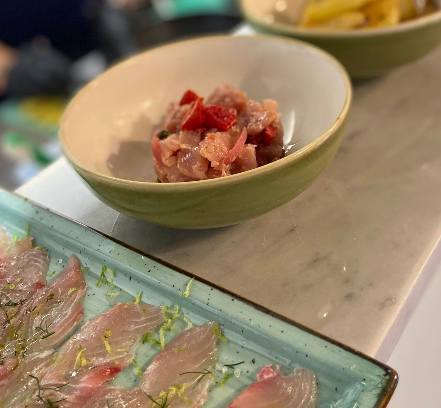 Piatto di frutti di mare: gamberi, carpaccio di pesce e tartare di tonno su un piatto blu.