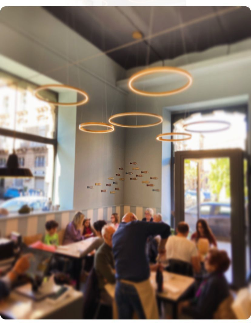 Interno del ristorante con tavoli e sedie, pareti in pietra anticata e parete decorativa a strisce con decorazioni a forma di pesce.