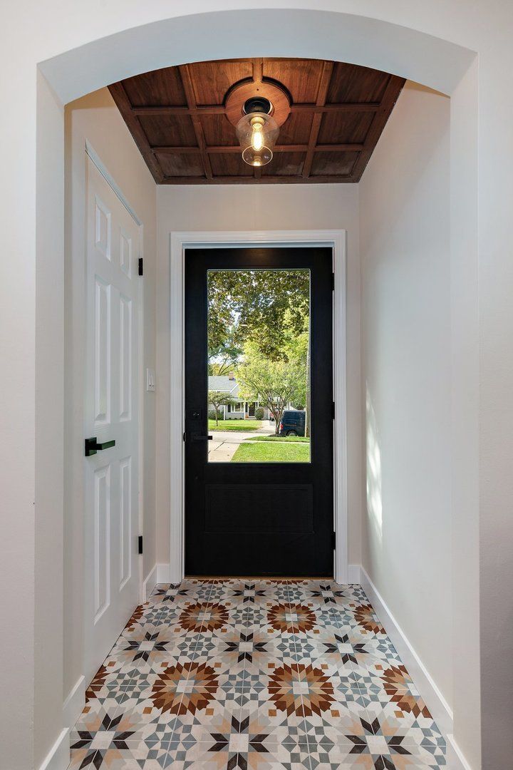 A hallway with a black door and a tiled floor.