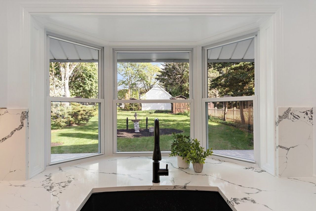 A kitchen sink with a view of the backyard through a bay window.