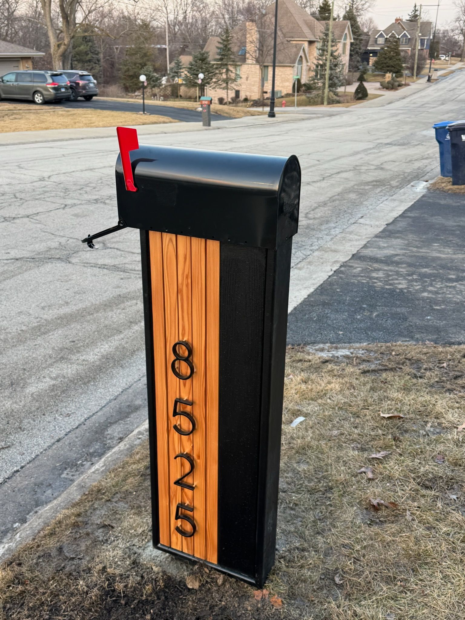 A black mailbox with a wooden plaque on it is on the side of the road.