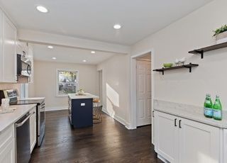 A kitchen with white cabinets , stainless steel appliances , hardwood floors and a blue island.
