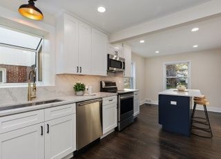 A kitchen with white cabinets , stainless steel appliances , a sink , and a blue island.