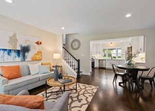 A living room with a couch , table , chairs and a clock on the wall.