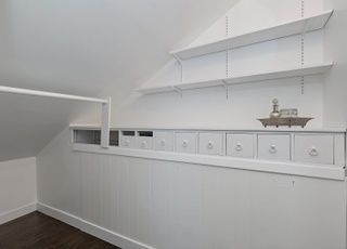 A room with a slanted ceiling and white shelves and drawers.