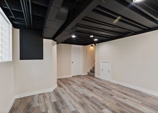 An empty basement with wooden floors and a black ceiling.