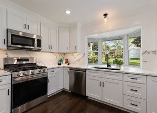 A kitchen with white cabinets , stainless steel appliances , and a large window.