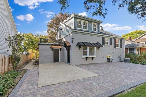 A large gray house with a brick driveway in front of it.