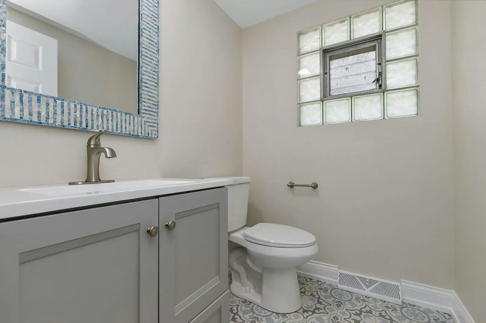 A bathroom with a toilet , sink , mirror and window.