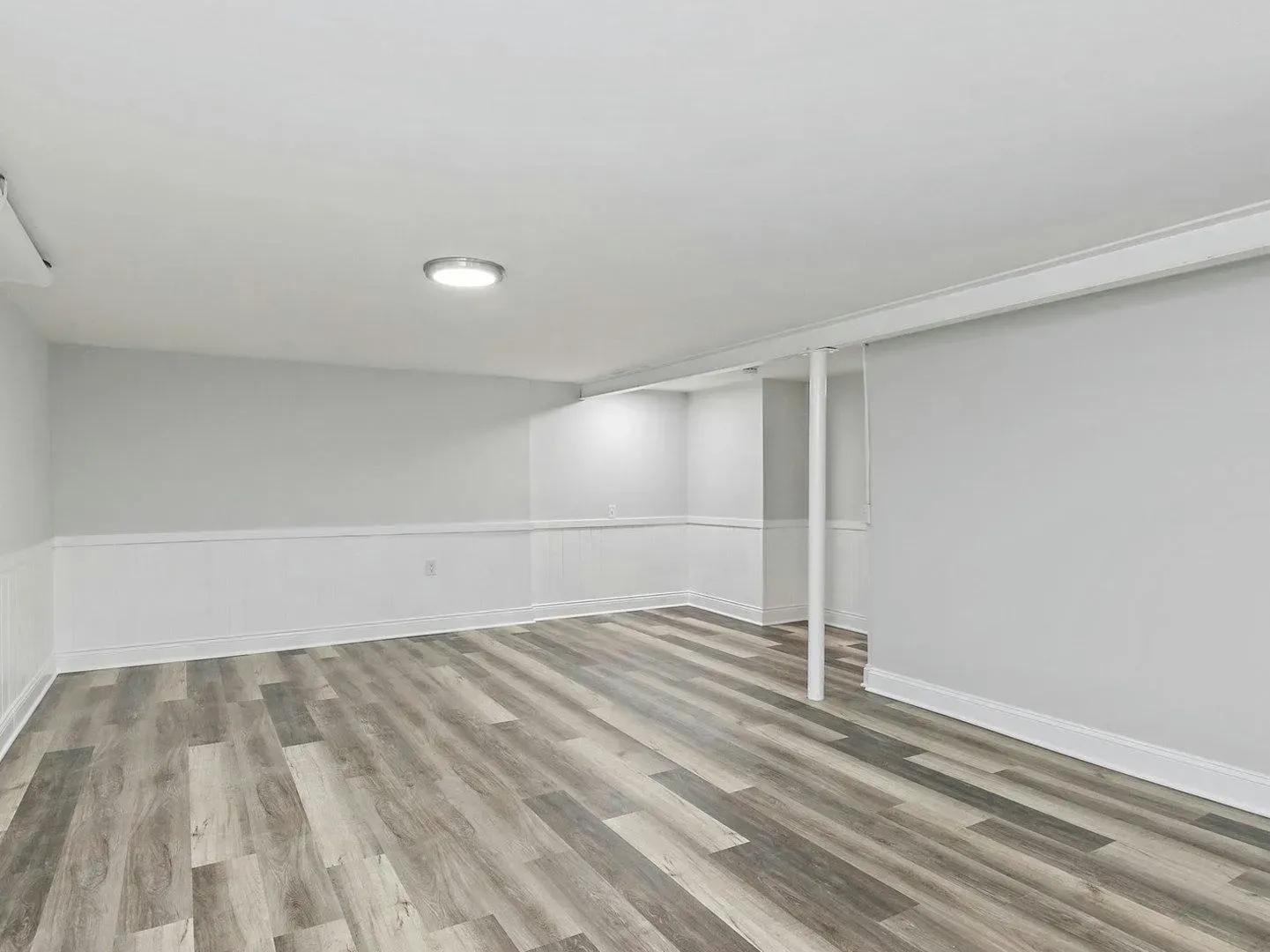 An empty basement with hardwood floors and white walls.