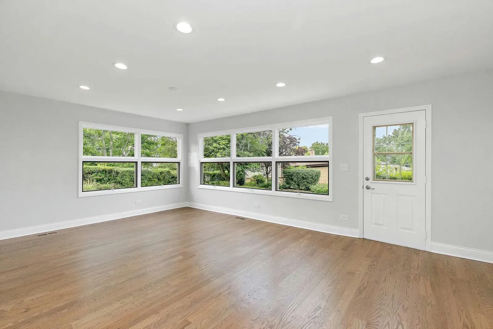 An empty living room with hardwood floors and lots of windows.