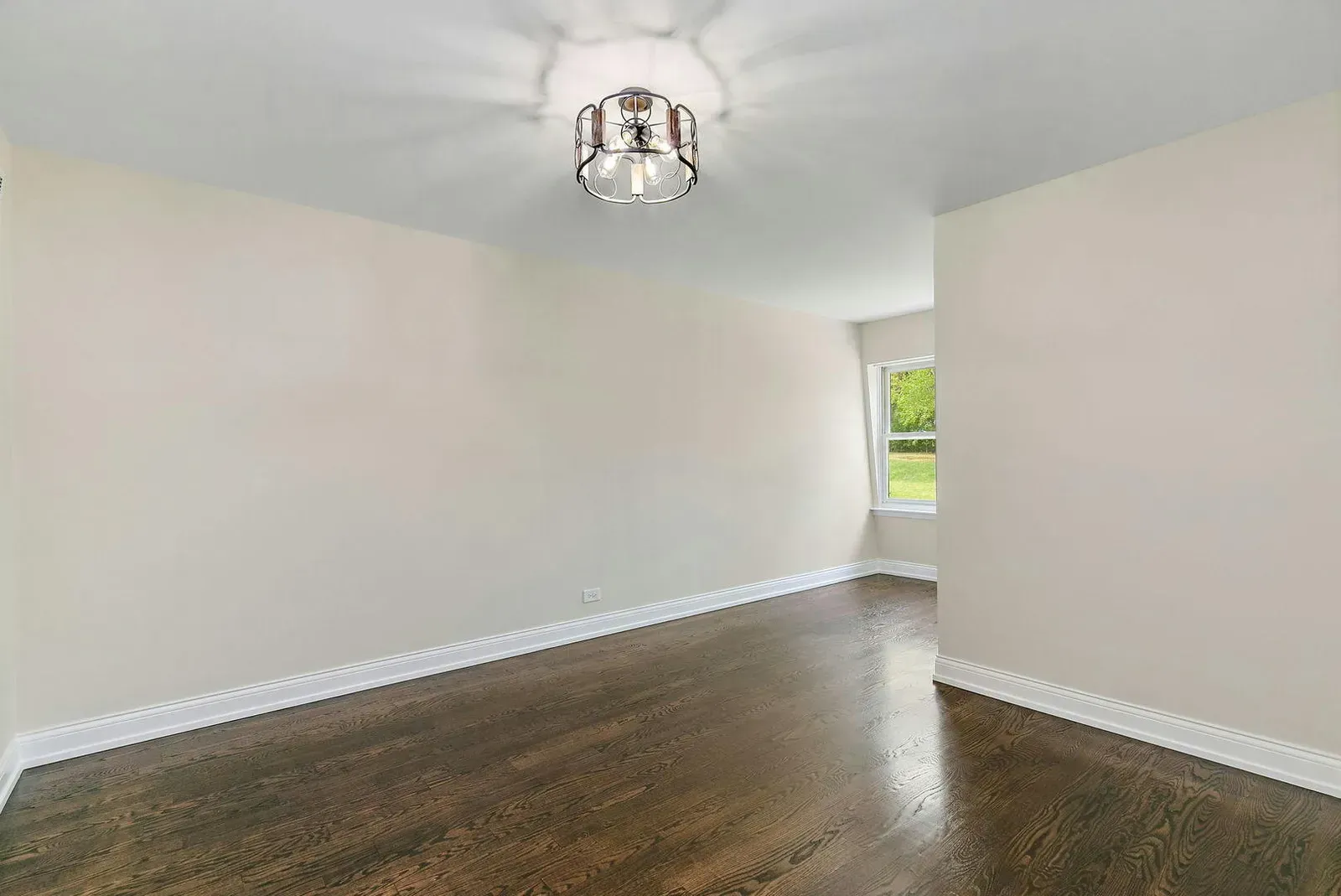 An empty room with hardwood floors , white walls and a chandelier.