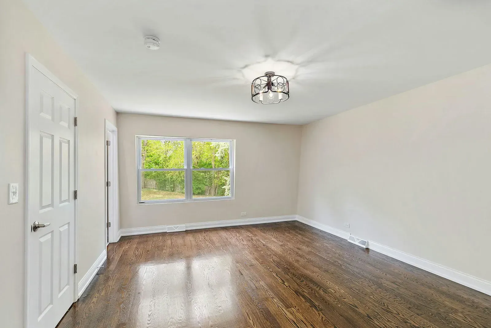 An empty living room with hardwood floors and two windows.
