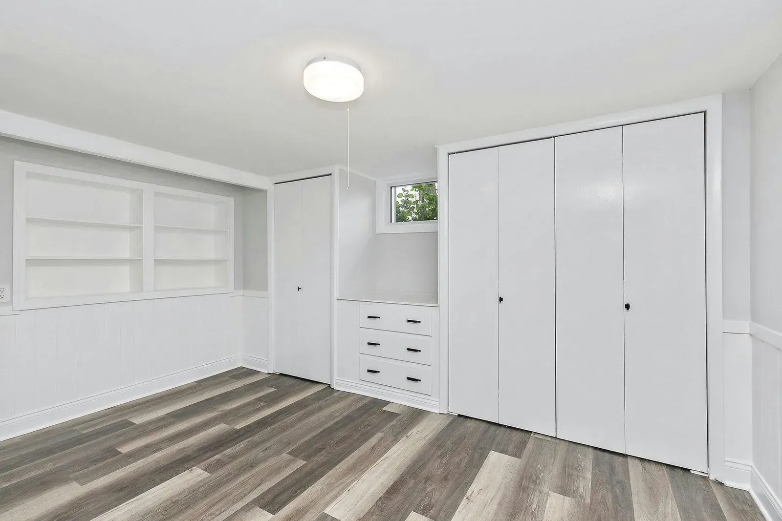 A bedroom with hardwood floors , white walls , and lots of closets.
