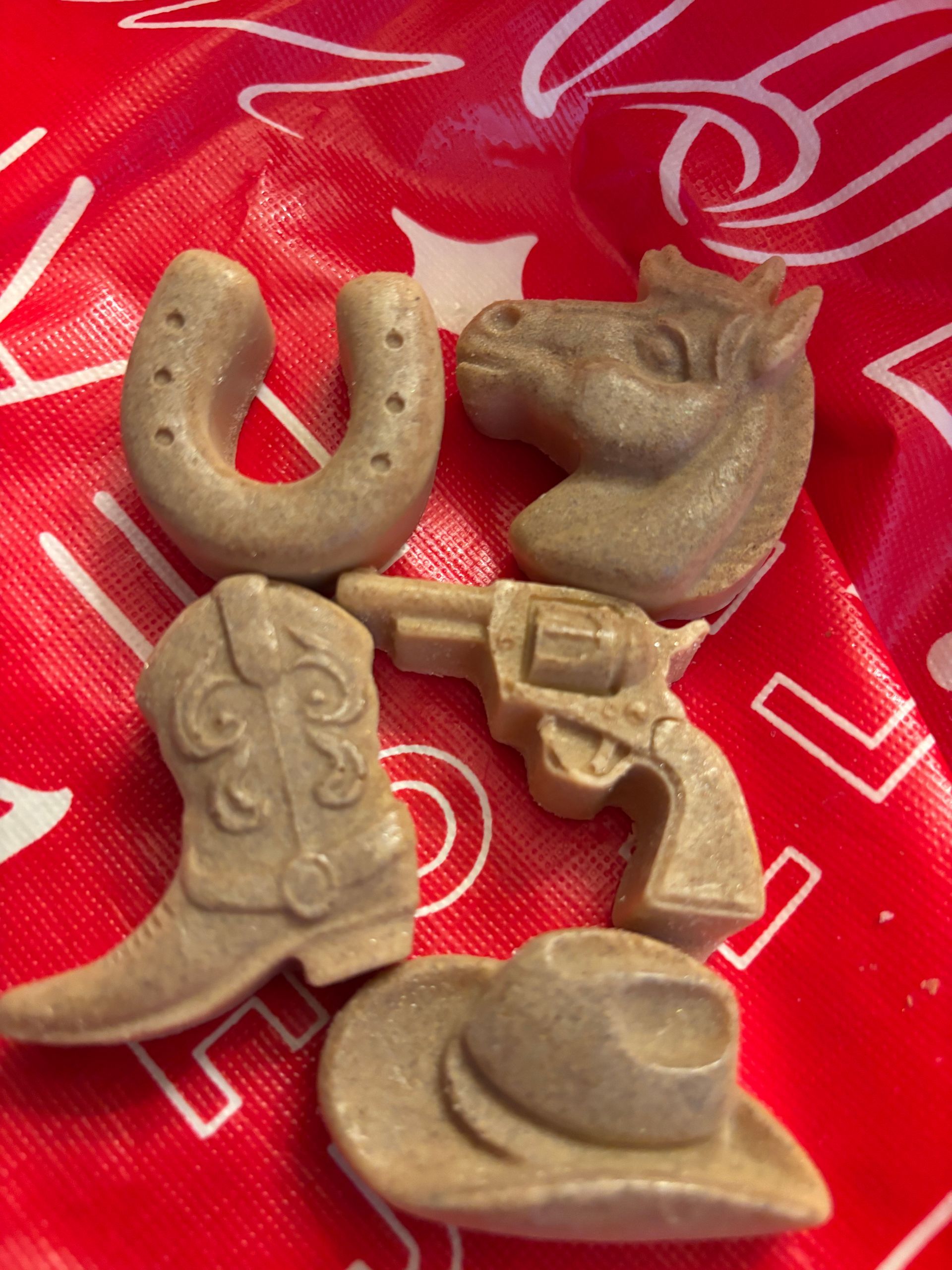 Five cowboy-themed candies: horseshoe, horse head, boot, revolver, and hat, on a red and white patterned background.