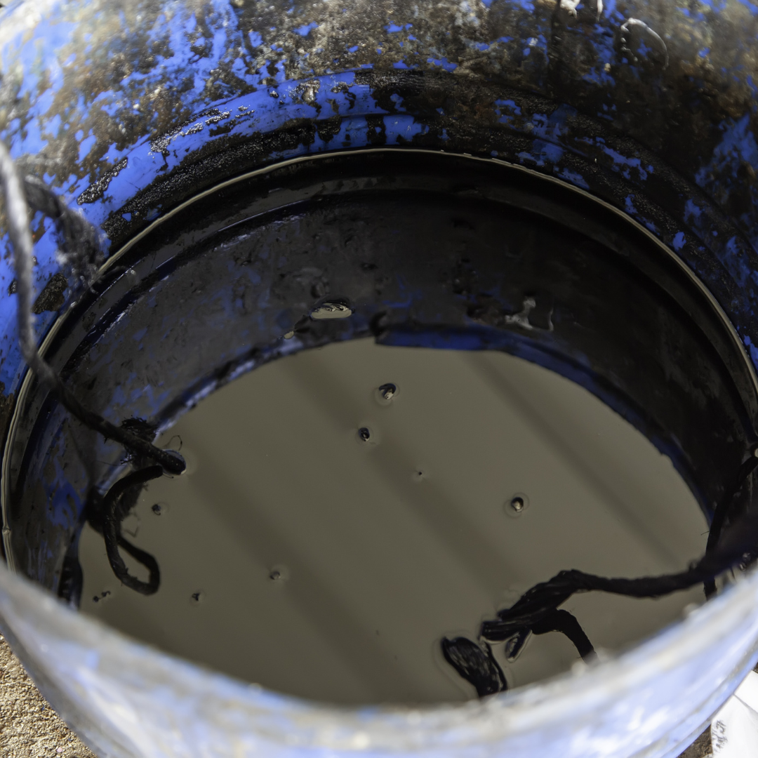 A blue bucket filled with black liquid with a rope sticking out of it