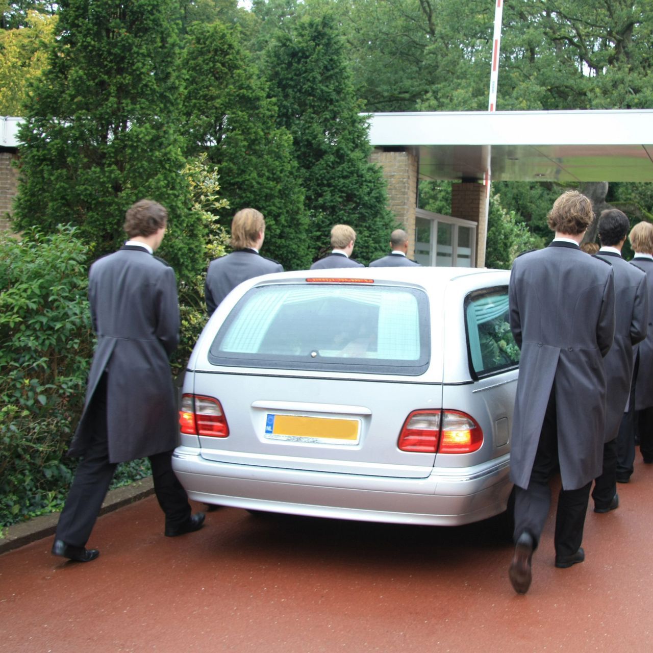 Un grupo de hombres de traje camina hacia un coche plateado.