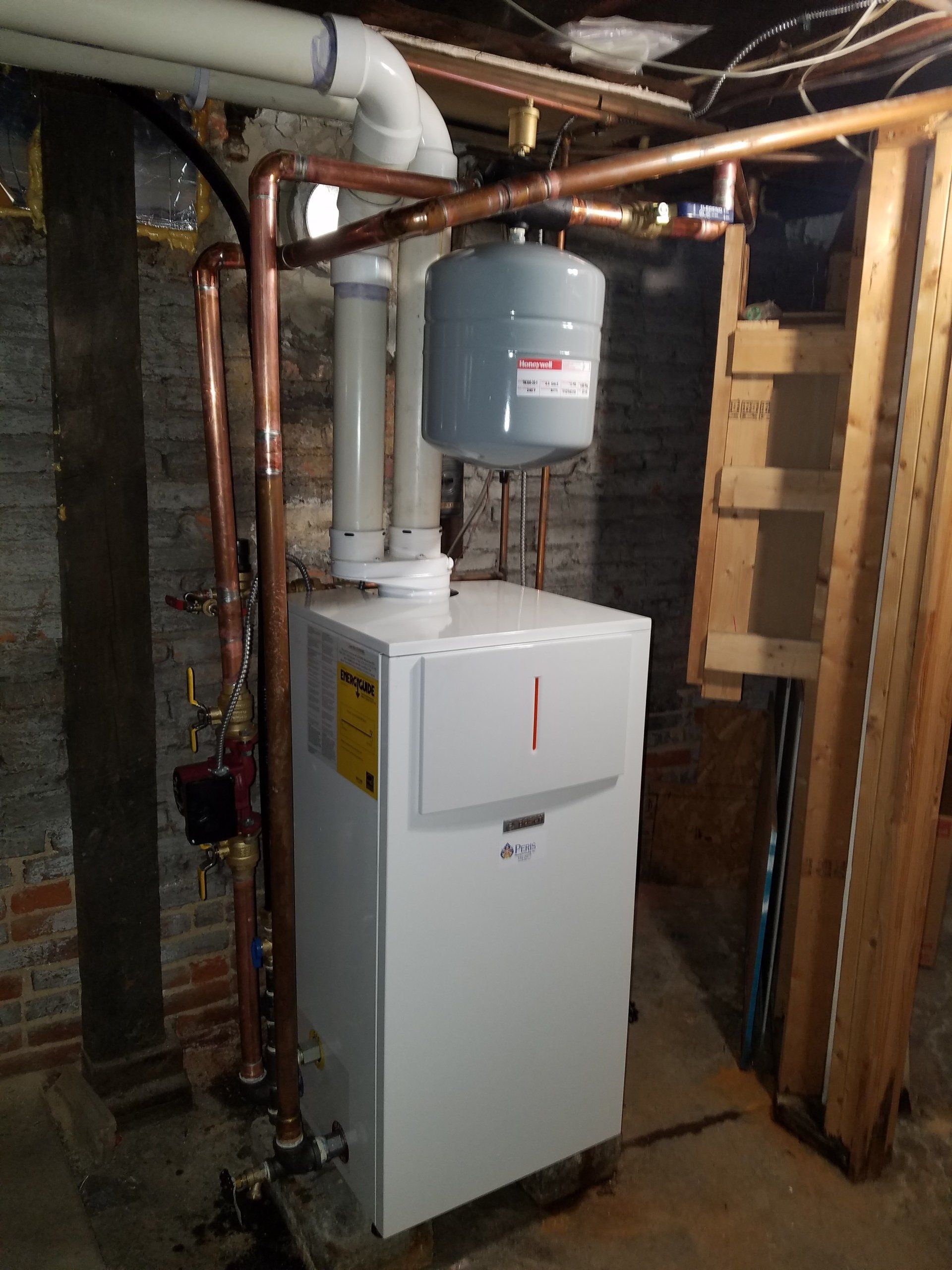 A white water heater is sitting in a basement next to copper pipes