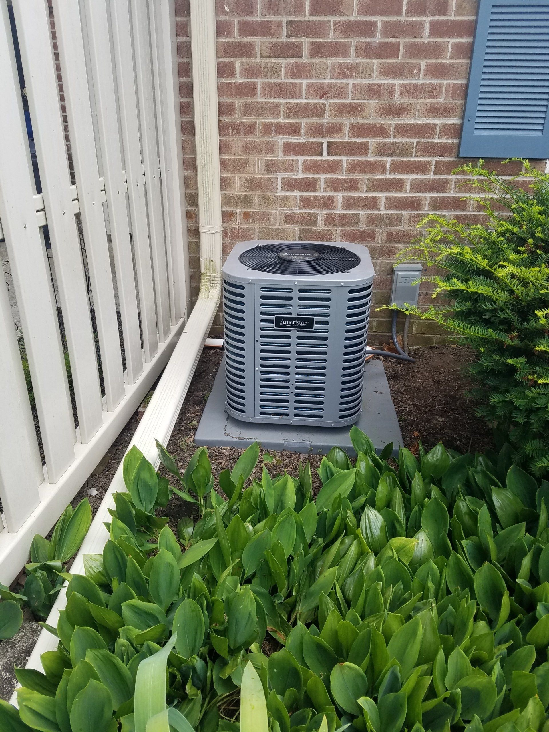 An air conditioner is sitting in a garden next to a brick wall.
