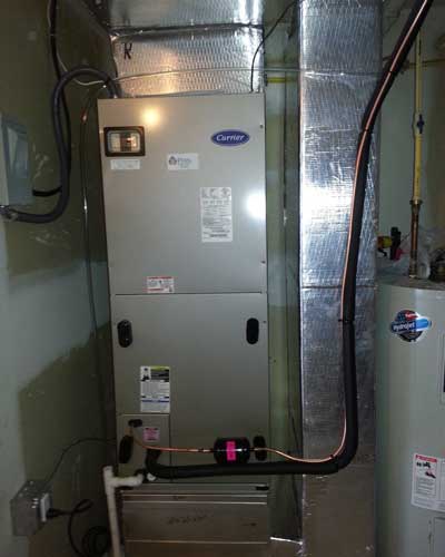 A carrier air conditioner is installed in a basement next to a water heater.