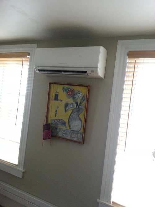 There is a picture of a vase on the wall above the air conditioner.