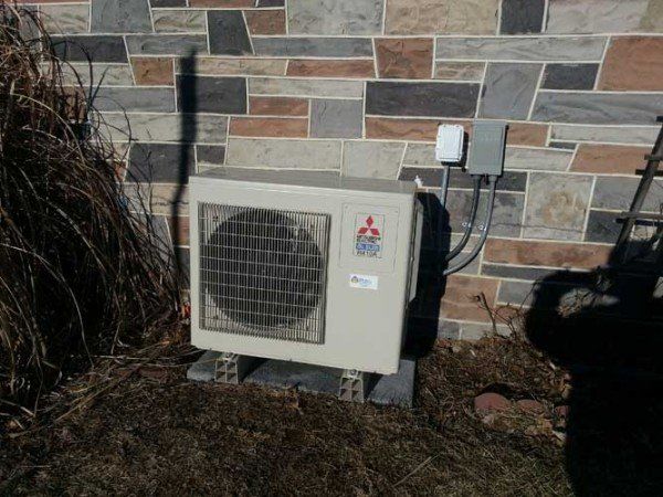 A mitsubishi air conditioner is sitting outside of a brick building.