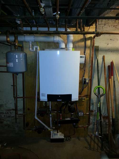 A white boiler is sitting in a basement next to pipes.